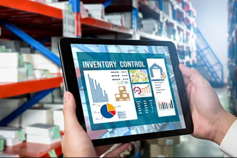 Hands holding tablet with inventory control charts in a warehouse with shelves and boxes in background