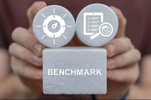 Hands holding blocks with a speedometer, checklist icons, and the word Benchmark on a foam block.