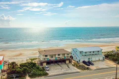 Oceanfront beach houses with parking, sandy shore, and calm sea under a partly cloudy sky at sunrise or sunset