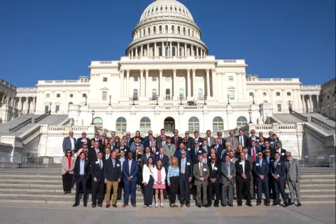 Group photo of diverse individuals in front of the United States Capitol building on a sunny day.