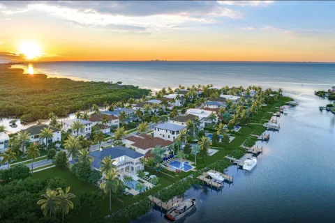 Sunset over modern waterfront homes with palm trees and boats along a canal near the ocean coastline.