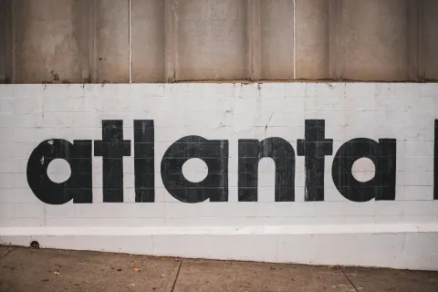 Black bold text reading atlanta painted on a white brick wall under a concrete section.