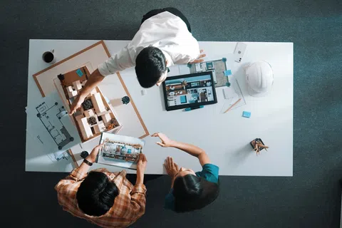 Three architects collaborating over blueprints and a building model at a white table in an office.