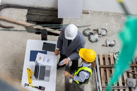 Construction manager and engineer reviewing project plans and data on site with laptop and documents.