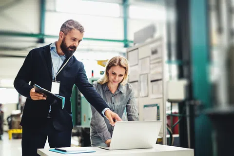 Man in suit explaining work to woman using laptop in modern industrial office environment