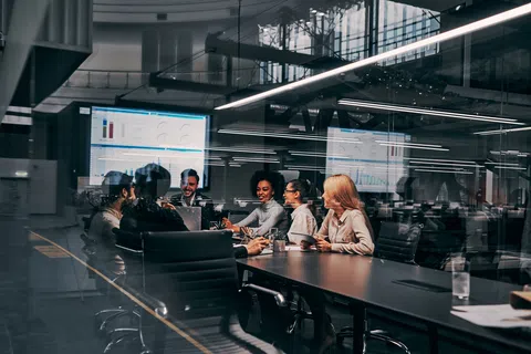 Diverse team in a modern conference room discussing data charts displayed on a large screen during a meeting.