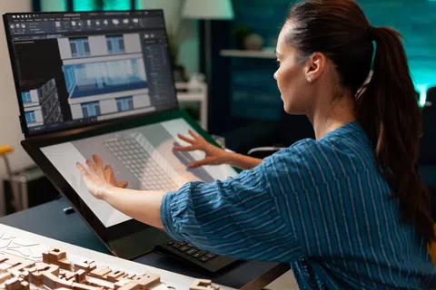 Woman using a large touchscreen monitor for architectural design work in a modern office setting