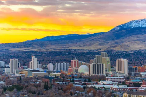 Cityscape of Reno Nevada with buildings and mountains at sunset under vibrant orange sky.