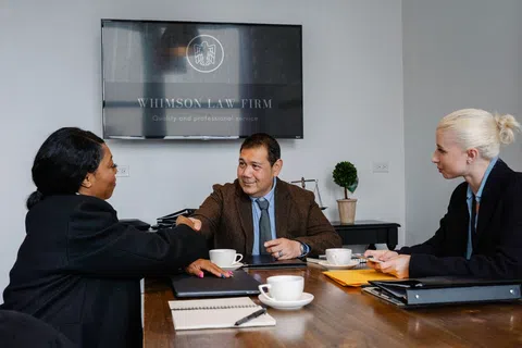 Lawyers at Whimson Law Firm shaking hands during a business meeting in a modern office conference room.
