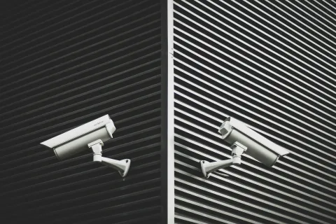 White security cameras mounted on opposite sides of a corner with black striped walls in the background