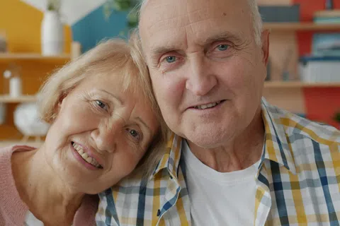 Smiling elderly couple sitting close together in a cozy, colorful living room environment