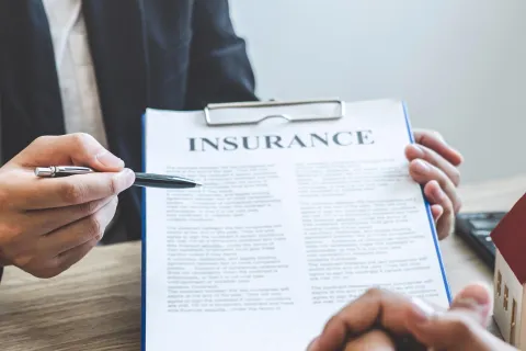 a person holding a pen and a paper with a house in the background