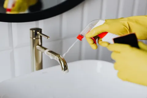 a person with gloves on cleaning the faucet of a sink