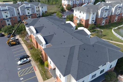 Aerial view of a multi-building student housing complex during commercial roof replacement by Mattco Group, with forklift loading materials onto an occupied residential property