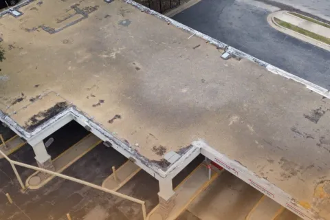 Aerial view of a flat, weathered commercial building roof with faded patches and surrounding parking area.
