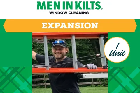 Smiling man in kilt holding a window cleaning ladder outdoors with green trees in the background