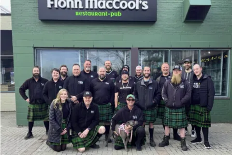 Group of people in kilts outside Fionn MacCool's restaurant-pub, smiling and posing together.