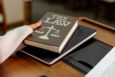 Person with pink nails holding a law book with scales of justice on cover over a desk with papers.