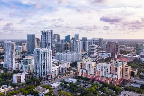 Aerial view of a modern city skyline with high-rise buildings and partly cloudy sky at dusk.