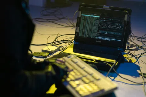 Person using a laptop displaying code and data with cables and keyboard in a dimly lit room.