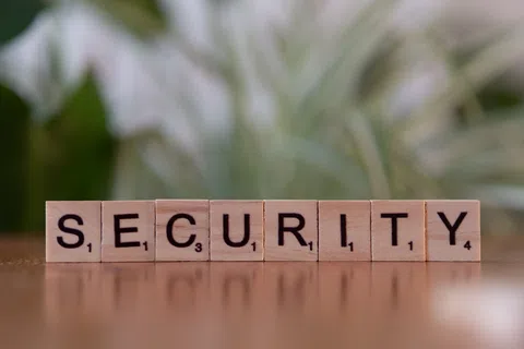 Wooden Scrabble tiles spelling the word SECURITY on a reflective surface with blurred green background.