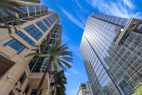 Low angle view of modern glass skyscrapers and palm trees under a blue sky with clouds.