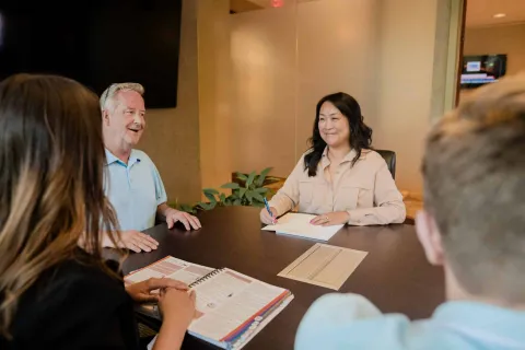 Four diverse colleagues engaged in a meeting around a conference table with documents and notebooks.