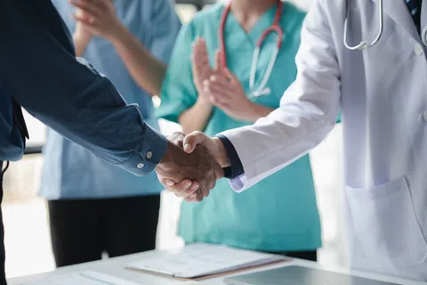 Doctor and patient shaking hands with medical staff applauding in background in healthcare setting.