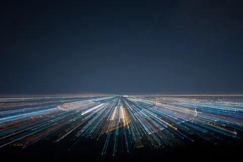 Night cityscape with streaks of blue and yellow lights converging towards the horizon under dark sky.