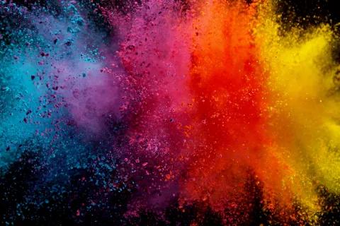 Vibrant blue, purple, red, orange, and yellow powder explosion on a black background creating a colorful burst.