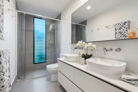 Modern bathroom with dual vessel sinks, large mirror, glass shower enclosure, frosted vertical window, and decorative orchid.