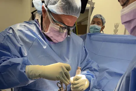 Surgeon wearing magnifying glasses and protective gear performing surgery in an operating room.