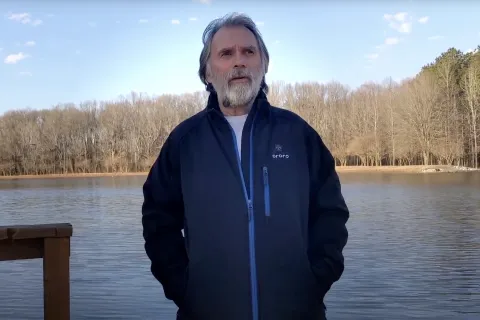 a man standing by a body of water with trees in the background
