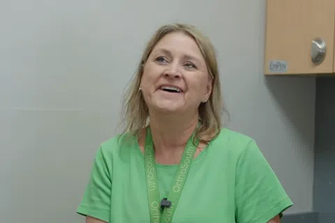 Smiling woman in a green shirt and OrthoSouth lanyard talking in an office setting
