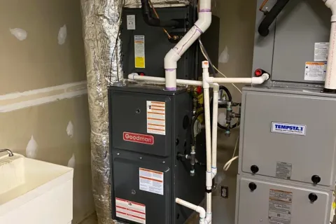 Basement HVAC system featuring Goodman and Tempstar furnaces with ductwork and plumbing beside a utility sink.