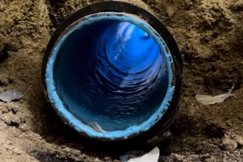 Close-up of a blue water pipe in soil with visible water flow inside surrounded by dirt and debris.