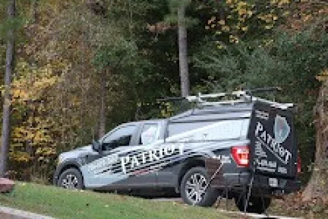 Patriot service truck parked on a grassy hill near trees and a small solar panel in autumn surroundings.