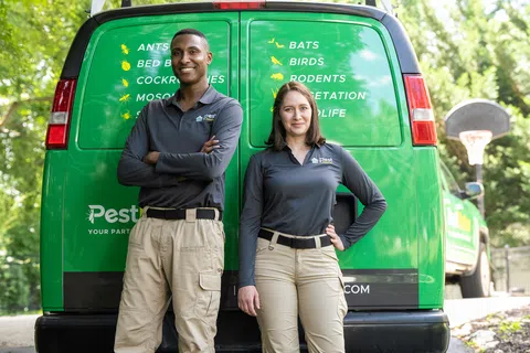 Two pest control technicians in uniform standing confidently in front of a green service van outdoors.