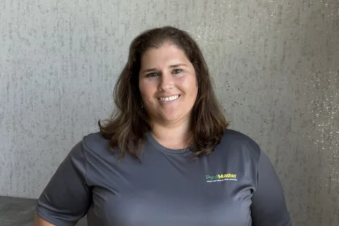 Smiling woman in grey PestMaster shirt standing against textured light wall