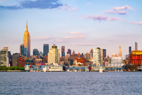 New York City skyline with the Empire State Building and waterfront under a blue sky with clouds.
