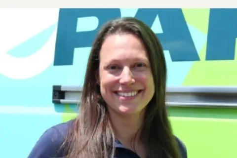 Smiling female franchise owner standing in front of branded vehicle with standout text above her.