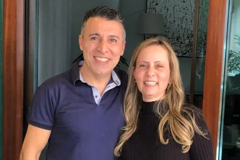 Smiling man and woman standing together inside a home near a glass door and artwork on the wall.