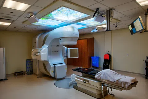 Medical radiotherapy room with advanced linear accelerator machine and patient treatment table covered with sheet
