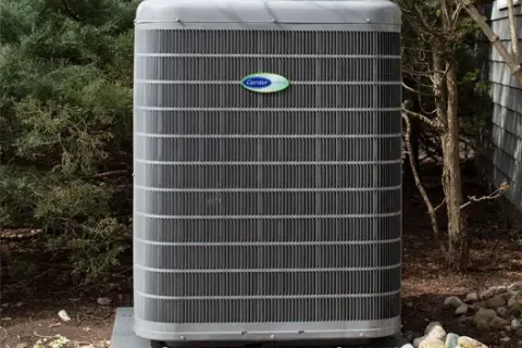 Outdoor Carrier air conditioning unit installed on concrete slab surrounded by rocks and greenery.