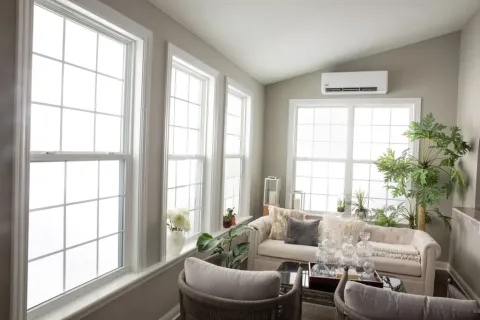 Bright living room with large windows, beige sofa, glass coffee table, and green indoor plants.