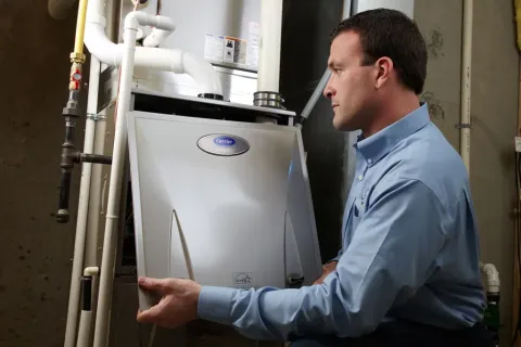 Technician inspecting and adjusting a Carrier Infinity HVAC system in a basement or utility room.