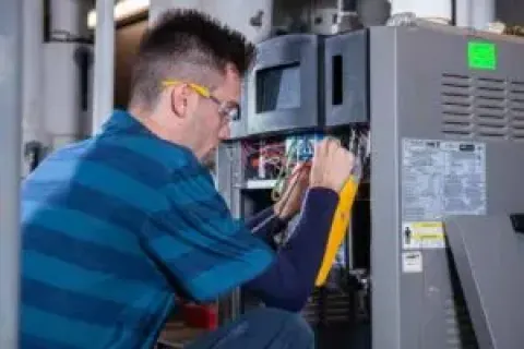 Technician wearing safety glasses working on wiring inside an industrial electrical panel or control box.