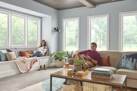 Couple relaxing in a bright living room with large windows, a wooden coffee table, and cozy seating area.