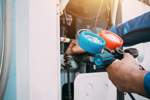 Technician using HVAC gauges to check air conditioning system pressure during maintenance work