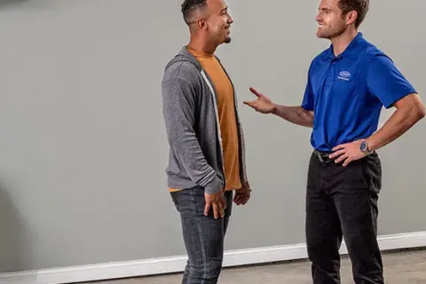 Technician and customer discussing air conditioner installation in a clean, empty room with concrete floor.